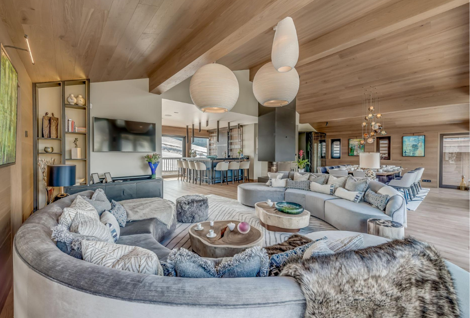 Chalet Bacchus in Courchevel 1650, the ideal chalet for a party ski holiday to celebrate a special occasion. Spacious living room, rounded sofas, slopes visible from the window, as well as a bar area and dining table.