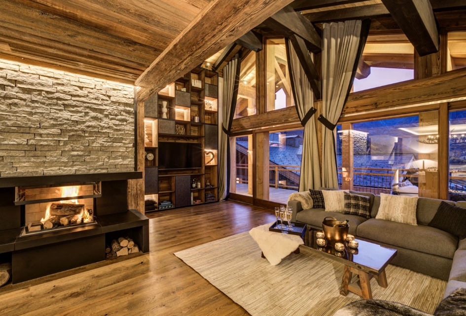 Cosy licing room with a fireplace and picture windows framing the evening mountain view at Chez Bugi, a ski in ski out chalet in St Martin de Belleville